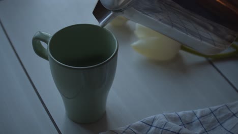 Gießen-Sie-Frischen-Tee-In-Einen-Becher-Auf-Einem-Holztisch-Mit-Weißer-Tulpenblume,-Nahaufnahme