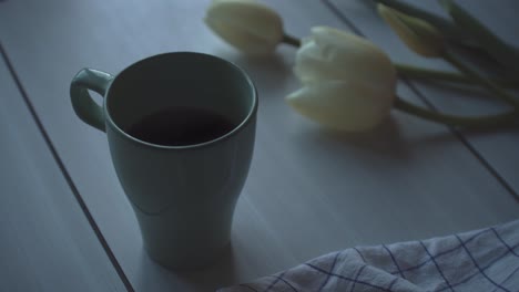 Teetasse-Auf-Holztisch-Mit-Tulpen-Und-Einem-Darauf-Ruhenden-Blatt