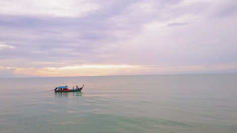 Drone-view-of-a-long-tail-boat-on-the-ocean-with-a-sunset-in-the-background