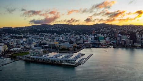 Aerial-hyperlapse,-sunset-over-New-Zealand-capital-Wellington-city-as-sun-begins-to-set-behind-the-hills,-pan-left
