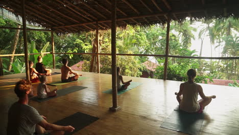 A-group-of-travelers-sitting-in-meditation-during-sunset-on-a-sunny-wooden-porch-overlooking-the-rainforest-and-jungle-leading-out-to-the-beach