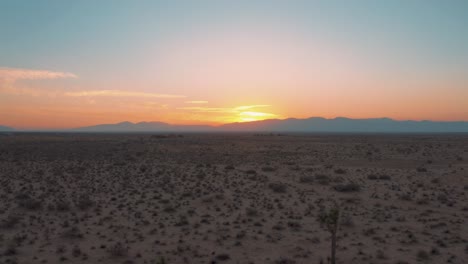 Flying-backward-through-Mojave-Desert-plain-during-colorful-sunset,-AERIAL