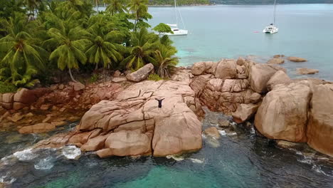 Aerial-drone-shot-of-a-lonely-but-happy-man-standing-on-a-small-tropical-islands-in-the-seychelles