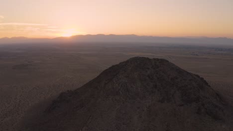 Aerial-orbit-around-Mojave-Desert-mountain-butte-during-pink-sunrise