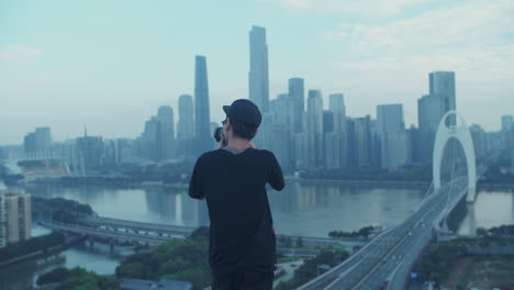 Open-shot-of-young-asian-photographer-capturing-urban-city-downtown-from-a-rooftop-in-the-early-morning