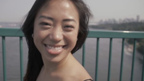 Close-up-shot-of-cute-asian-girl-doing-funny-smiling-face-at-Lions-Gate-bridge-in-Vancouver,-Slowmo