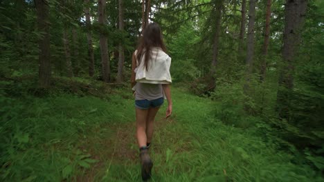 First-person-view-with-camera-shake-walking-through-the-woods-following-behind-a-tall-brunette-woman-on-a-hike