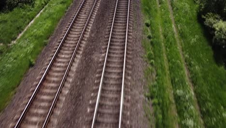 Endless-railway-tracks-surrounded-with-green-forest,-tilting-up-drone-view