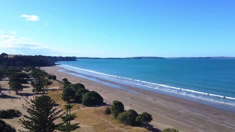 drone-shot,-flying-over-trees-towards-a-beautiful-beach-on-a-sunny-day-in-Long-Bay,-New-Zealand