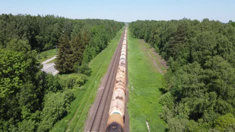 Following-endless-cargo-train-in-vibrant-green-landscape,-aerial-drone-view