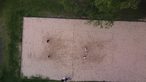 Group-of-women-playing-volleyball-on-sandy-surface,-top-down-aerial-view