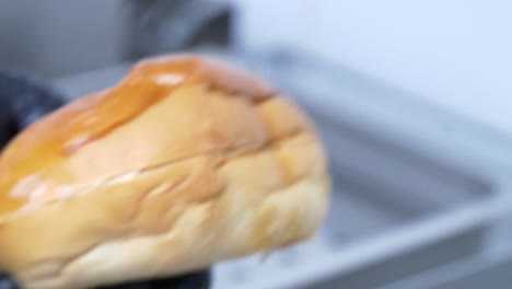 Close-up-of-a-hamburger-bun-being-sliced-in-half-by-hands-wearing-black-latex-gloves-for-food-safety-in-a-restaurant