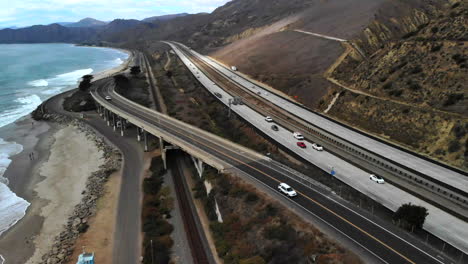 Aerial-drone-shot-over-the-top-of-a-concrete-bridge-on-the-beach-in-Ventura-next-to-the-ocean-waves-and-the-California-101-freeway-along-the-coast