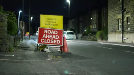 Road-closed-sign-with-traffic-passing-by-at-night