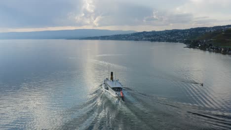 Aerial-shot-following-Belle-Epoque-steam-boat-on-Lake-Léman-in-front-of-Cully,-Lavaux---Switzerland-Mirror-like-water-and-storm-clouds-in-the-background