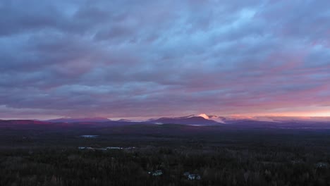 Aerial-footage-flying-backwards-at-sunrise-over-a-late-fall-forest-with-misty-mountains-in-the-distance