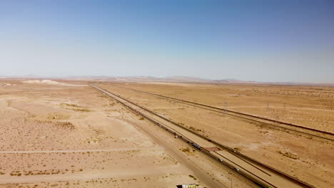 Aerial-view-of-a-long-straight-highway-stretching-through-a-barren-dessert-on-a-sunny-day