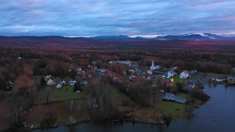 Aerial-footage-flying-over-lake-at-sunrise-in-late-fall-towards-small-rural-community-with-misty-mountains-in-the-distance