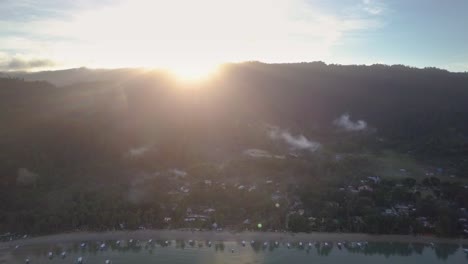 Aerial-of-fishing-village-with-sun-rising-behind-hilltop-in-the-Philippines---tracking-shot