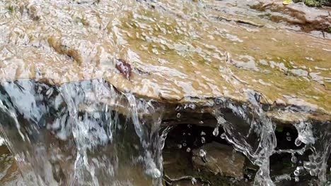 flowing-waterfall-from-a-mountain-spring-water-stream-running-down-huge-sandstone-slabs-of-rock-with-green-moss,-crystal-clear-drinking-water,-meditate-tranquil-and-peaceful-calm-slow-motion-footage