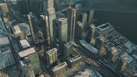 Aerial-view-of-tall-buildings-in-downtown-Toronto,-and-a-frozen-Lake-Ontario-during-a-cold-sunny-winter-afternoon