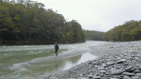 Woman-in-hiking-gear-walking-alongside-river-in-a-valley-on-New-Zealand's-South-Island