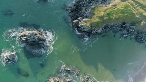 Top-down-aerial-tracking-from-right-to-left-out-from-a-golden-sandy-beach-along-the-turquoise-ocean-and-waves-of-the-Sutherland-coast-in-Northern-Scotland