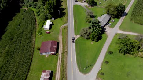 Aerial-view-of-country-road-with-cars-commuting-with-cornfields-and-trees-surrounding-on-a-nice-sunny-day