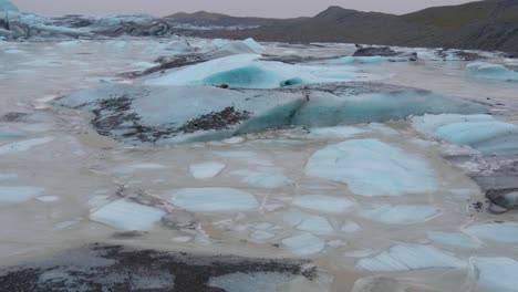 Estática,-Toma-De-Pequeños-Icebergs-Turquesas,-En-El-Glaciar-Skaftafellsjokull,-Montañas-Nevadas-En-El-Fondo,-En-Un-Día-Nublado,-En-La-Costa-Sur-De-Islandia