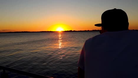 Kamerafahrt-Eines-Mannes,-Der-Auf-Einem-Deck-Den-Fluss-Bei-Sonnenuntergang-Betrachtet