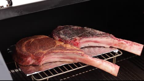 Two-raw-tomahawk-steaks-seasoned-and-spice-rub-on-the-smoker-grill-tilt-up-Concept:-BBQ,-Smoker,-outside-grilling,-food-preparation-cookout,-meat,-ribs-steaks