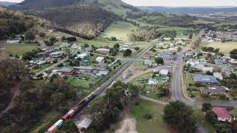 Drone-Rise-Up-Following-Train-Passing-Through-Country-Town-in-Tasmania,-Australia
