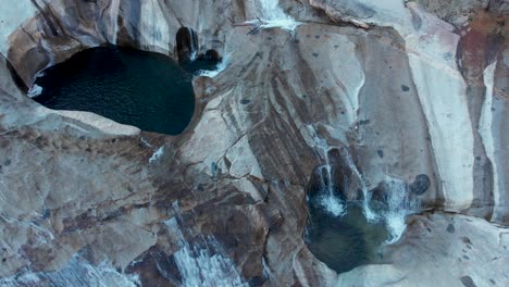 Top-down-aerial-shot-of-cascading-waterfalls-and-pools-on-a-granite-rock-face