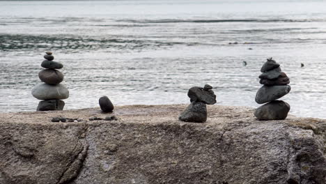A-group-of-cairns-stacked-on-a-large-boulder-with-a-calm-saltwater-bay-in-the-background