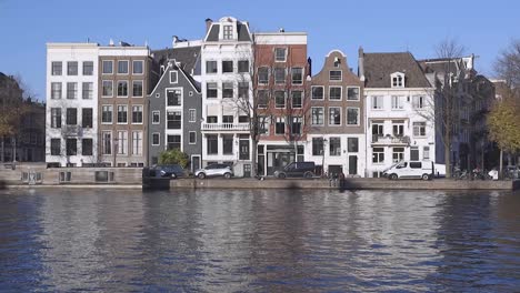 Typical-canal-houses-in-Amsterdam,-The-Netherlands,-reflecting-in-the-canal-in-front-on-a-sunny-day-with-blue-sky