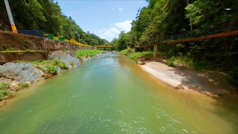 Racing-drone-flying-under-bridge-on-Jimenoa-river-at-Jarabacoa,-Dominican-Republic