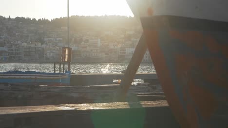 Slider-shot-off-bow-of-carvel-fishing-boat-pier-focusing-on-sunlit-water-and-Greek-town