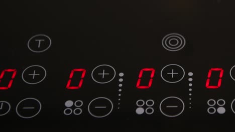 Close-up-of-electric-stove-control-panel,-red-illuminated-LED-indicators-on-black-surface,-home-appliances,-kitchen-stove,-slow-pan-right-to-left,-mid-sequence-display-change,-finger-pressing-buttons
