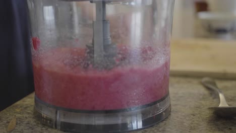 Closeup-of-a-person-is-using-a-blender-to-mix-raspberries-in-a-kitchen