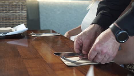 Male-waiter-putting-cutlery-on-wooden-table-while-young-blond-hair-woman-looking-at-menu-in-luxury-restaurant---Low-Close-Up