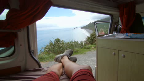 POV-out-of-a-campervan-to-a-awesome-seascape,-a-blonde-girl-walks-in-front-of-the-car,-Westcoast,-New-Zealand