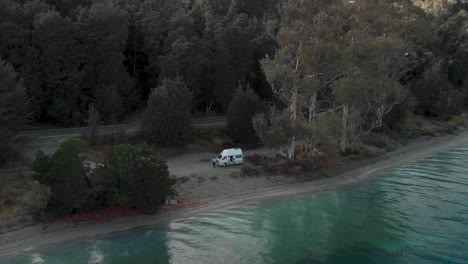 SLOWMO---Campervan-on-beach-beautiful-blue-Lake-Wakatipu,-Queenstown,-New-Zealand-and-trees-scenery-during-fall-autumn---Aerial-Drone