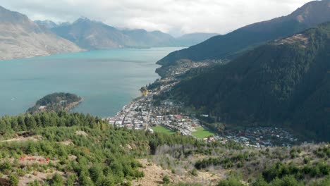 Beautiful-view-of-Queenstown-from-Queenstown-Hill-track-hike,-New-Zealand-and-Lake-Wakatipu,-mountains-with-fresh-snow,-clouds-and-town---Aerial-Drone