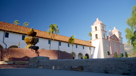 The-historic-Santa-Barbara-Mission-with-a-fountain-and-the-red-tile-roof-and-Spanish-catholic-architecture-in-California-with-palm-trees