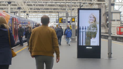 Digital-vertical-advertising-display-at-a-major-railway-station-with-passengers-boarding-a-train