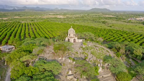 Drone-view-of-San-Martin-de-Porres-shrine-on-hill-next-to-mango-farm,-Bani,-Dominican-Republic