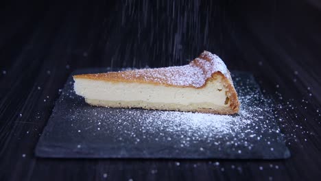 Pouring-sugar-on-slice-of-cheesecake-on-stone-plate-close-up-shoot-slow-motion