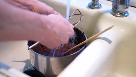 A-chef-cleaning-up-and-washing-the-dishes,-bowls-and-utensils-that-are-covered-in-chocolate-cake-batter-after-baking-in-the-sink