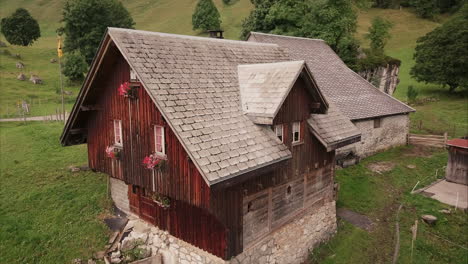 romantic-wooden-farm-house-in-the-swiss-mountains,-aerial-drone-flight