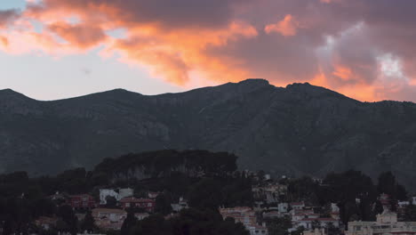 Zooming-in-timelapse-of-huge-clouds-moving-fast-over-and-behind-a-mountain-during-sunset